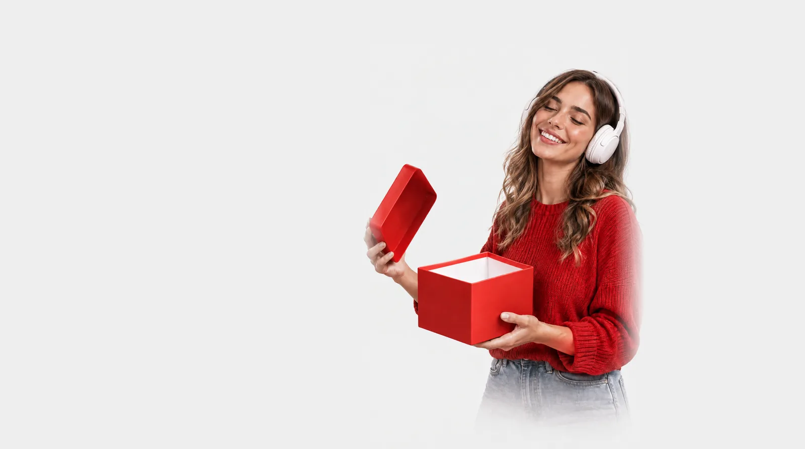 Mujer con auriculares sonriendo mientras abre una caja de regalo roja
