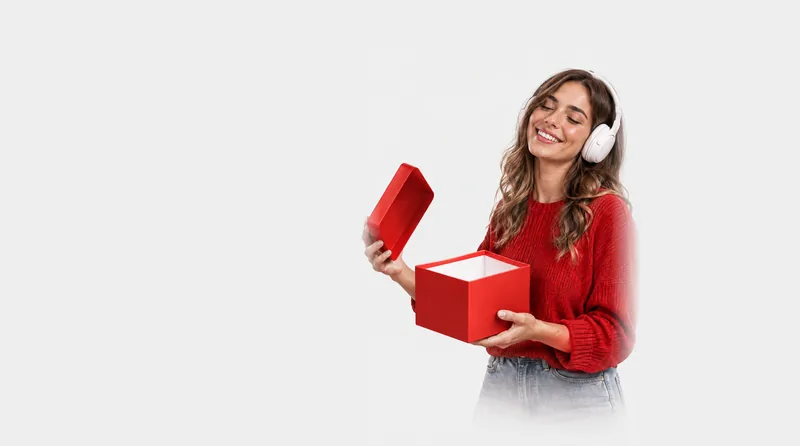 Mujer con auriculares sonriendo mientras abre una caja de regalo roja